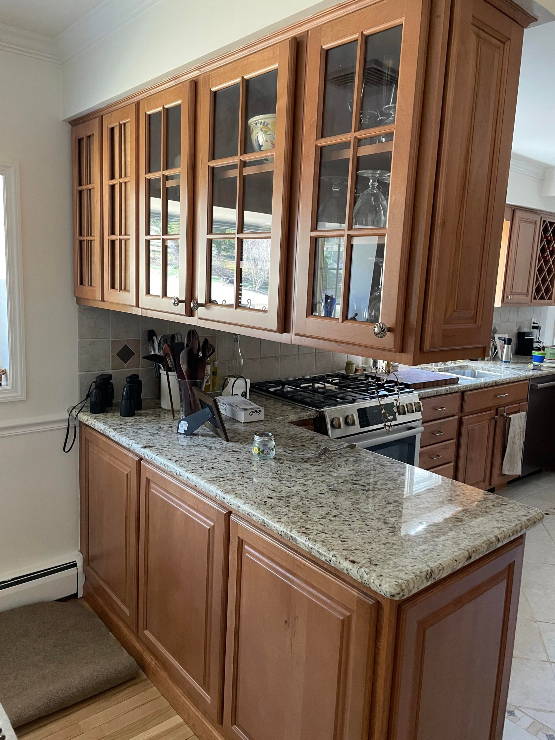 Wide view of a kitchen with honey oak cabinets, mullion glass upper doors, speckled granite counters, and a tile floor.