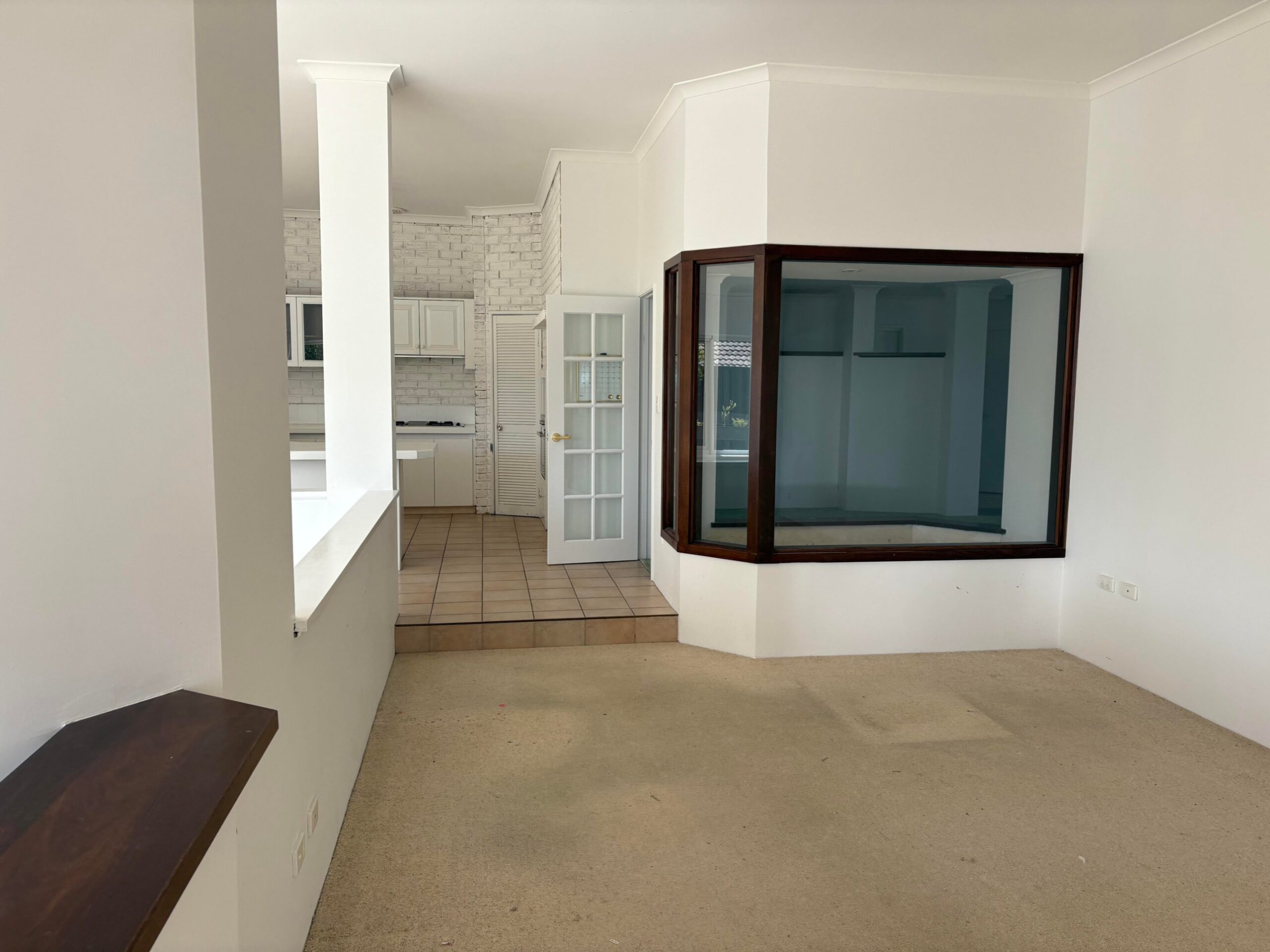 Dated kitchen with white painted brick walls, cream tile floor, white laminate cabinets, and an odd glass box built into the wall used as an indoor garden display.