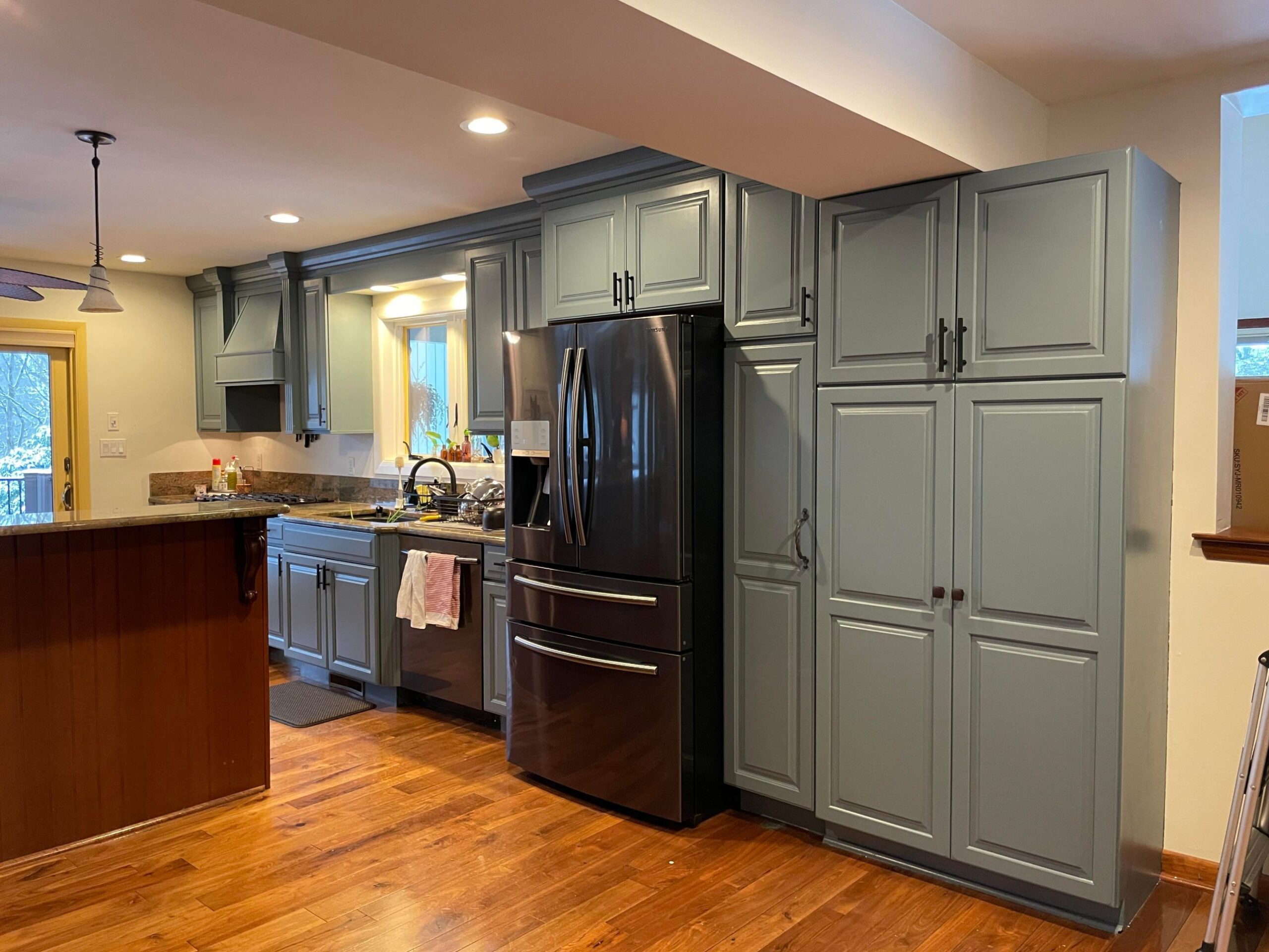 Deep slate blue cabinets wrapping around the black Samsung fridge, with the previously cherry pantry tower now painted the same blue, creating a unified built-in look.