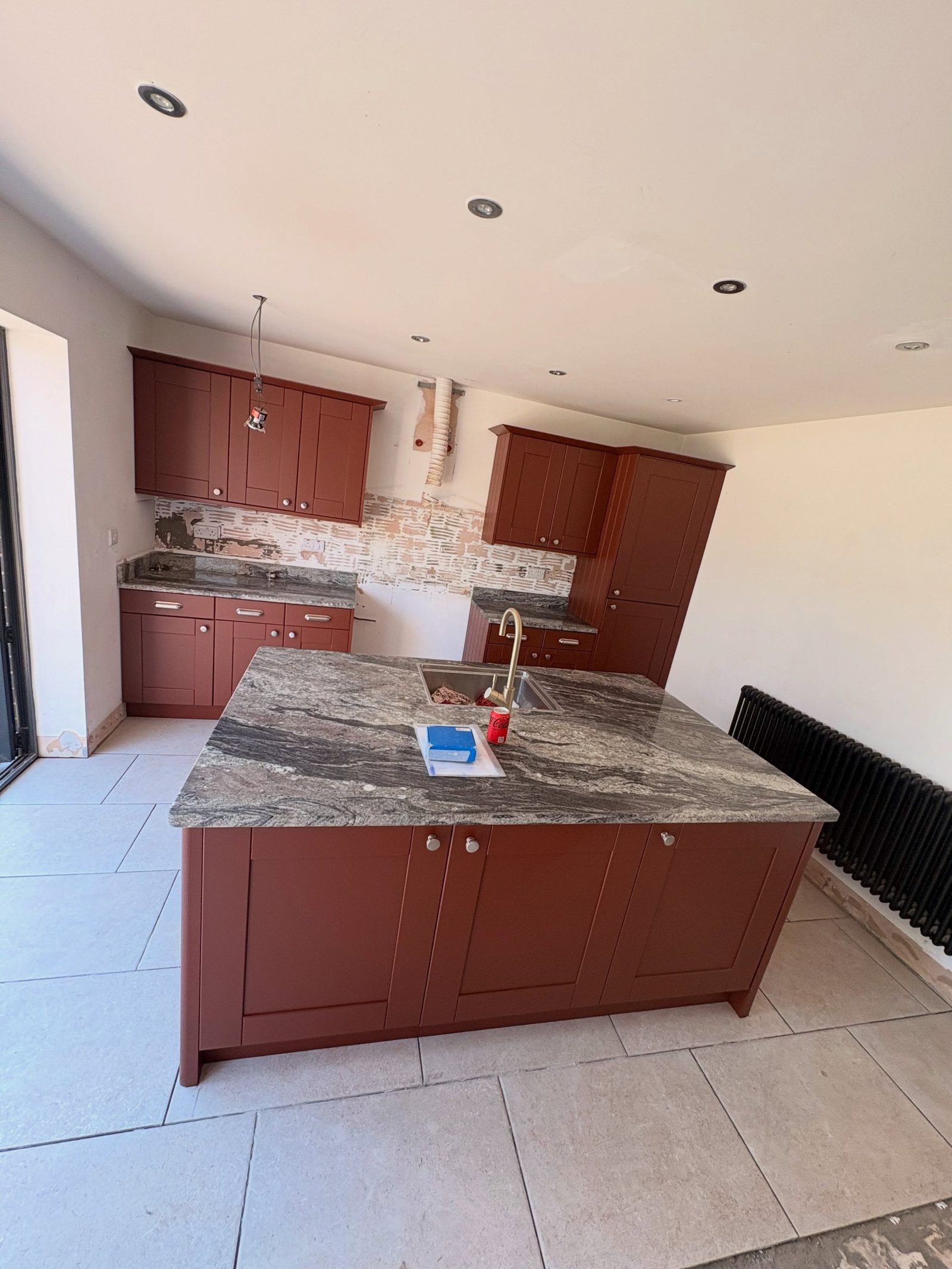 Finished Etruscan Red lower cabinets with the kept green-gray granite worktop and bare plaster where the old tile backsplash came off.