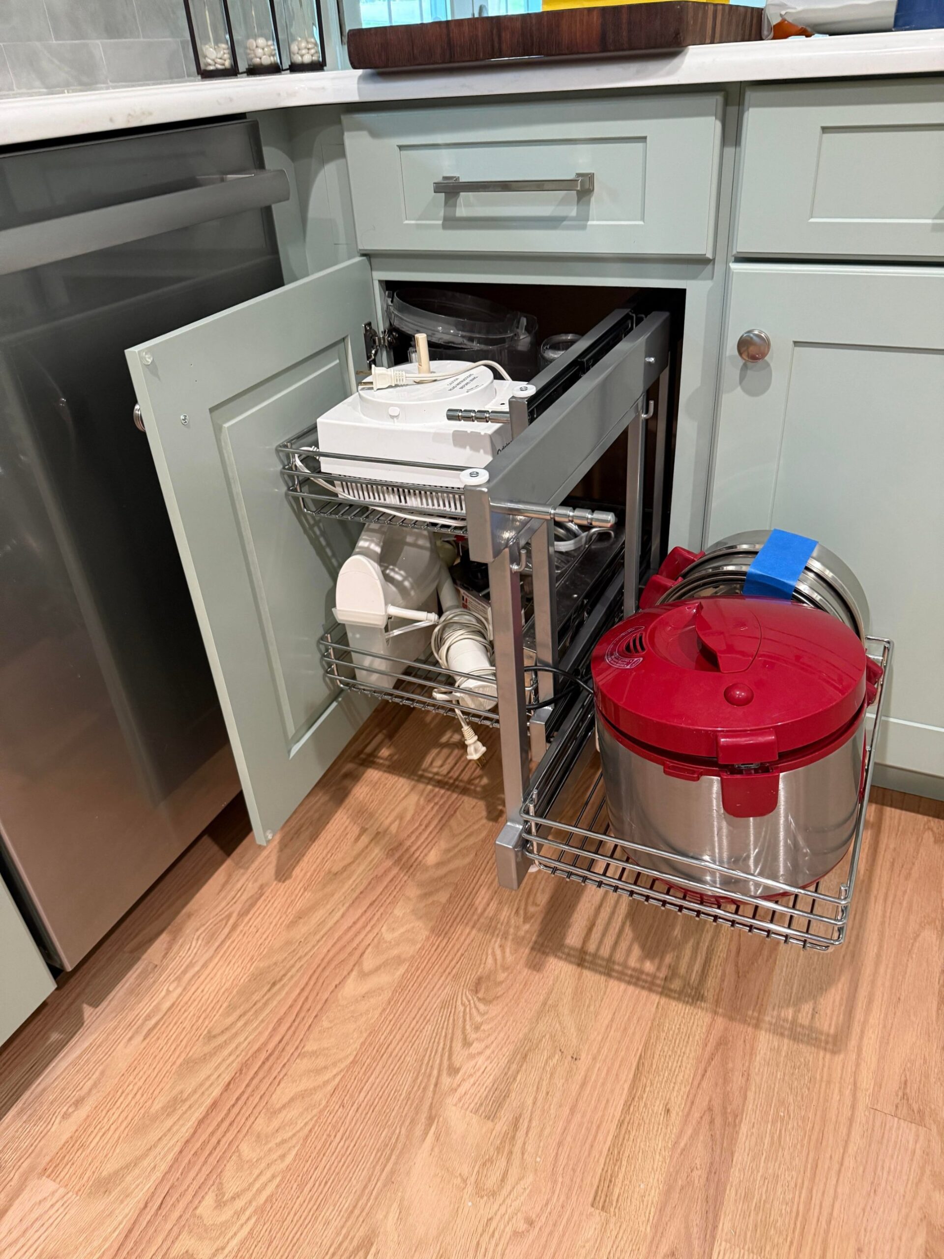 Open blind-corner cabinet with a two-tier chrome Rev-A-Shelf pullout extended out, holding a stand mixer base and a stainless and red pressure cooker.