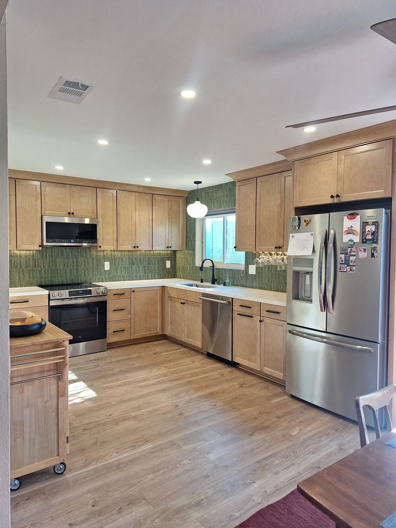 Finished L-shaped kitchen with rye-stained maple Shaker cabinets, honed quartz counters, matte black hardware, a stainless electric range with over-range microwave, and a green vertical fluted ceramic backsplash.