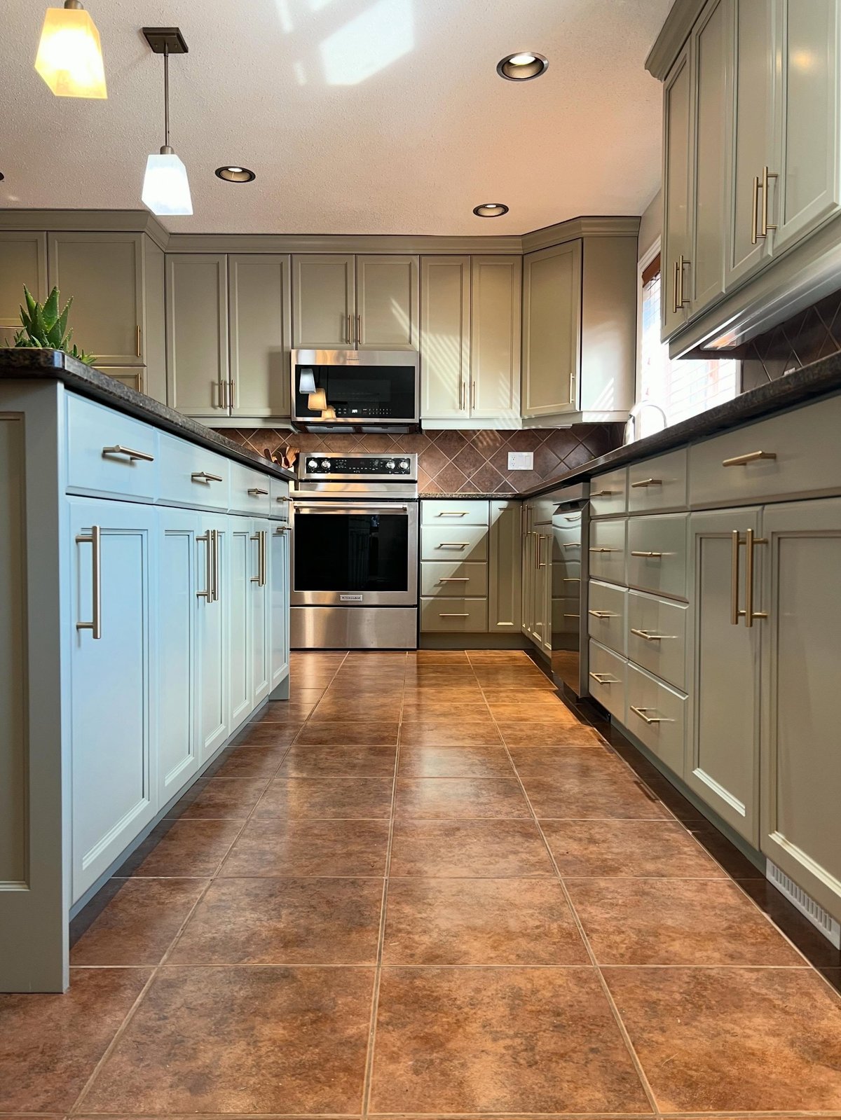 Same kitchen galley after the makeover, sage green painted cabinets on both sides with brass bar pulls, the same brown diamond backsplash and brown granite counters still in place.