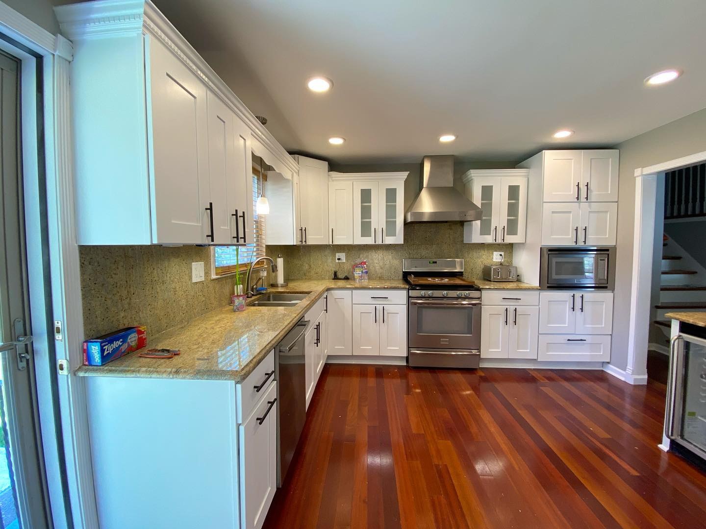 Same U-shaped kitchen with cabinets now painted Sherwin-Williams Extra White, matte black bar pulls, the original granite counters and Brazilian cherry floors still in place.