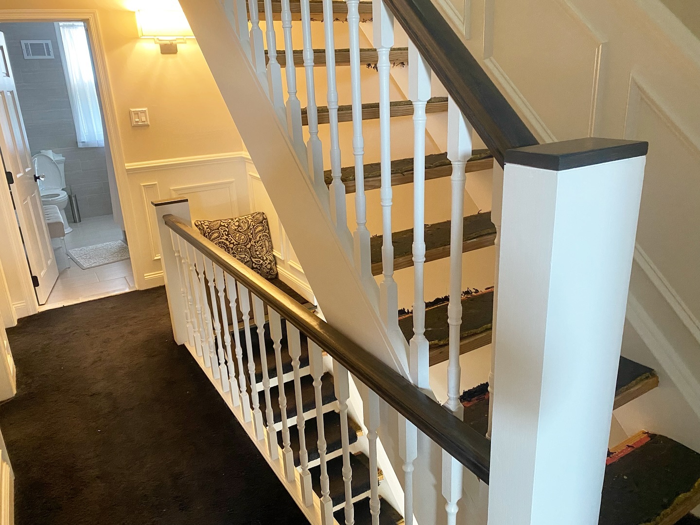 Mid-project view with finished white spindles and a dark stained handrail, stair treads partially stripped of carpet and padding to show the bare wood underneath.