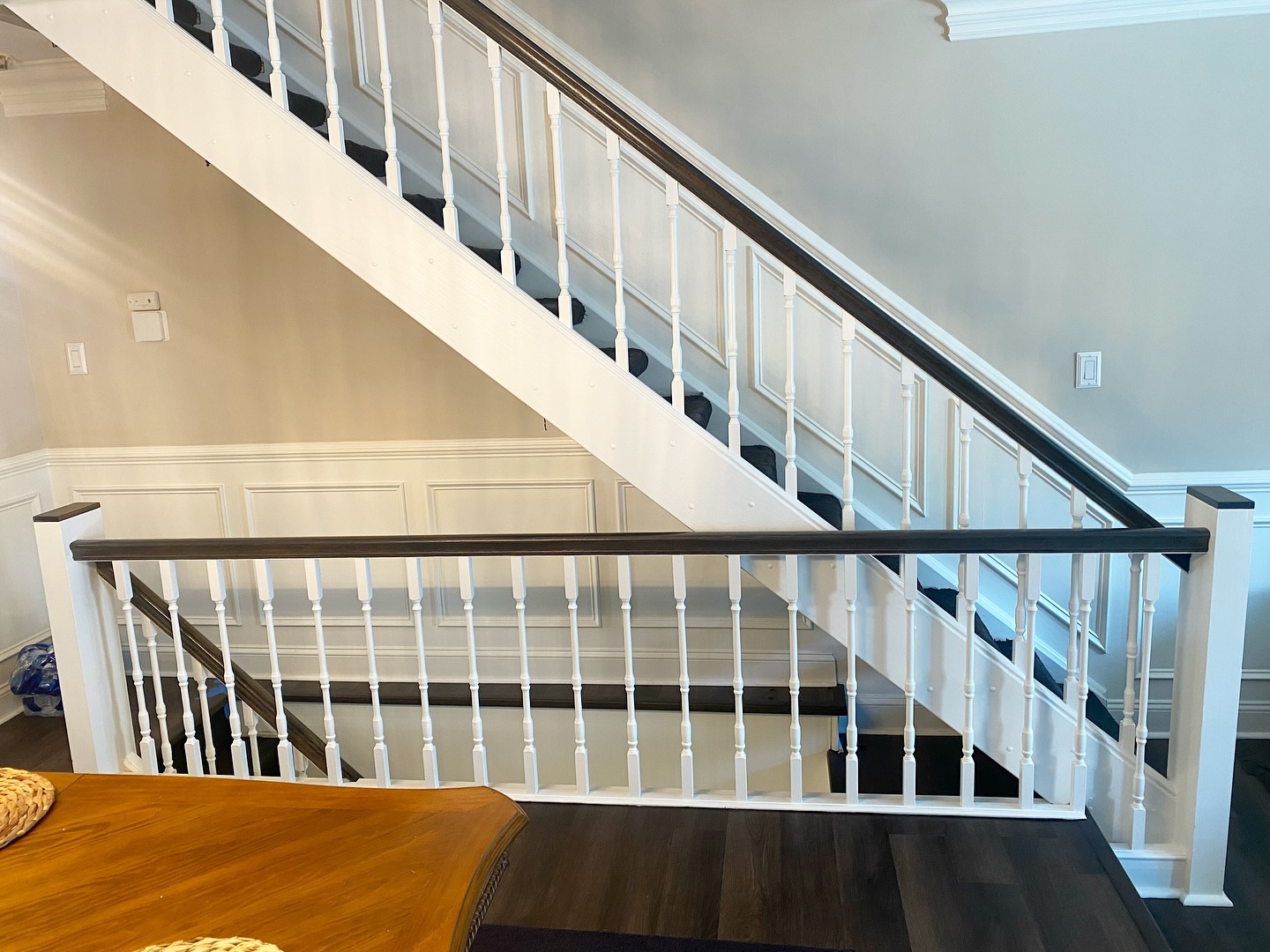 Finished staircase landing with white spindles, dark stained handrail cap and dark wood floor framing the dining room beyond.