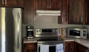 Dark walnut shaker kitchen cabinets with a stainless LG fridge, white range hood, and tan speckled laminate counters, shot before a Sherwin-Williams Accessible Beige paint refresh.