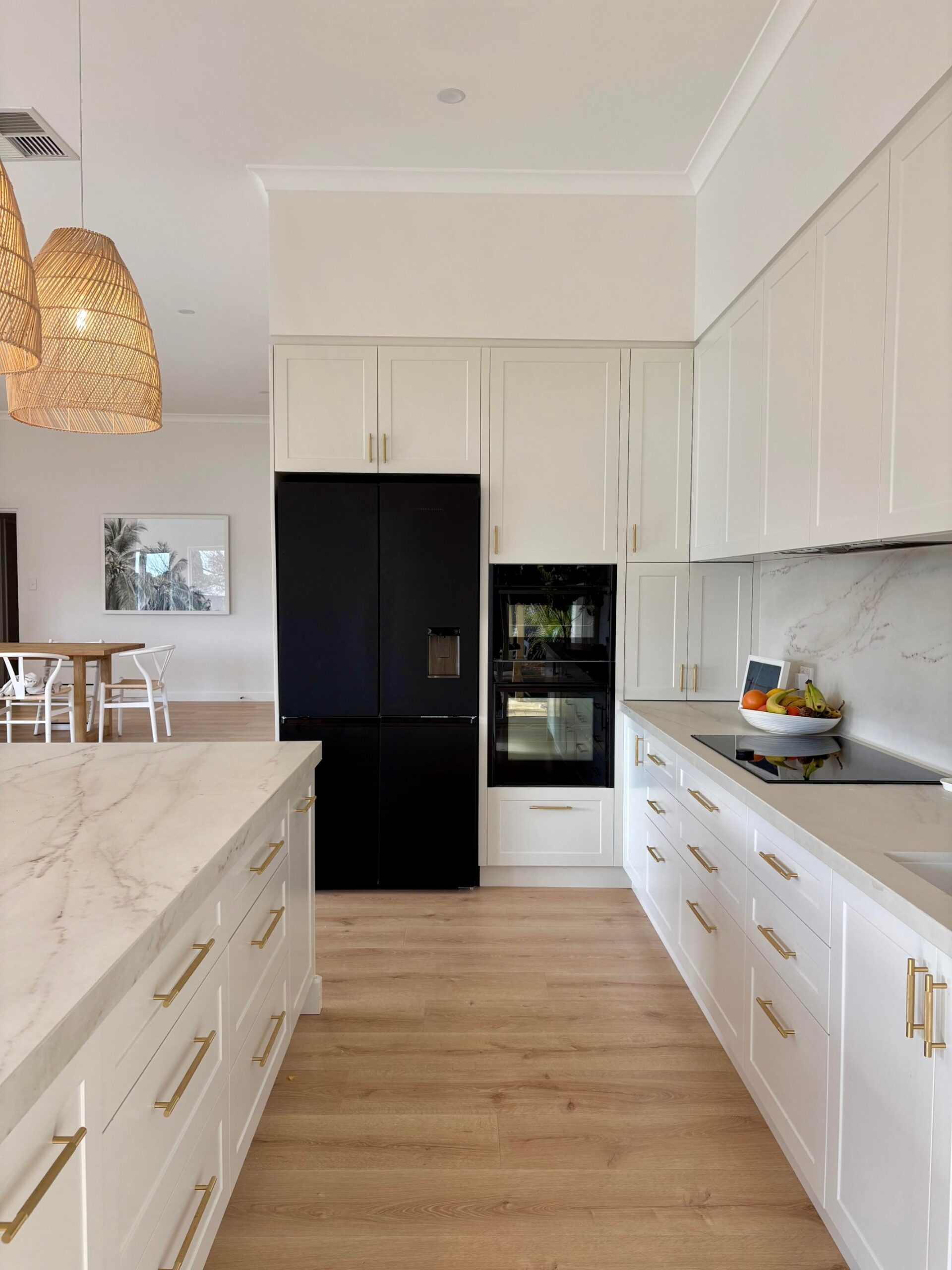 White Shaker kitchen with a black French door fridge, built-in double wall oven, cream Dekton counters, and gold hardware.