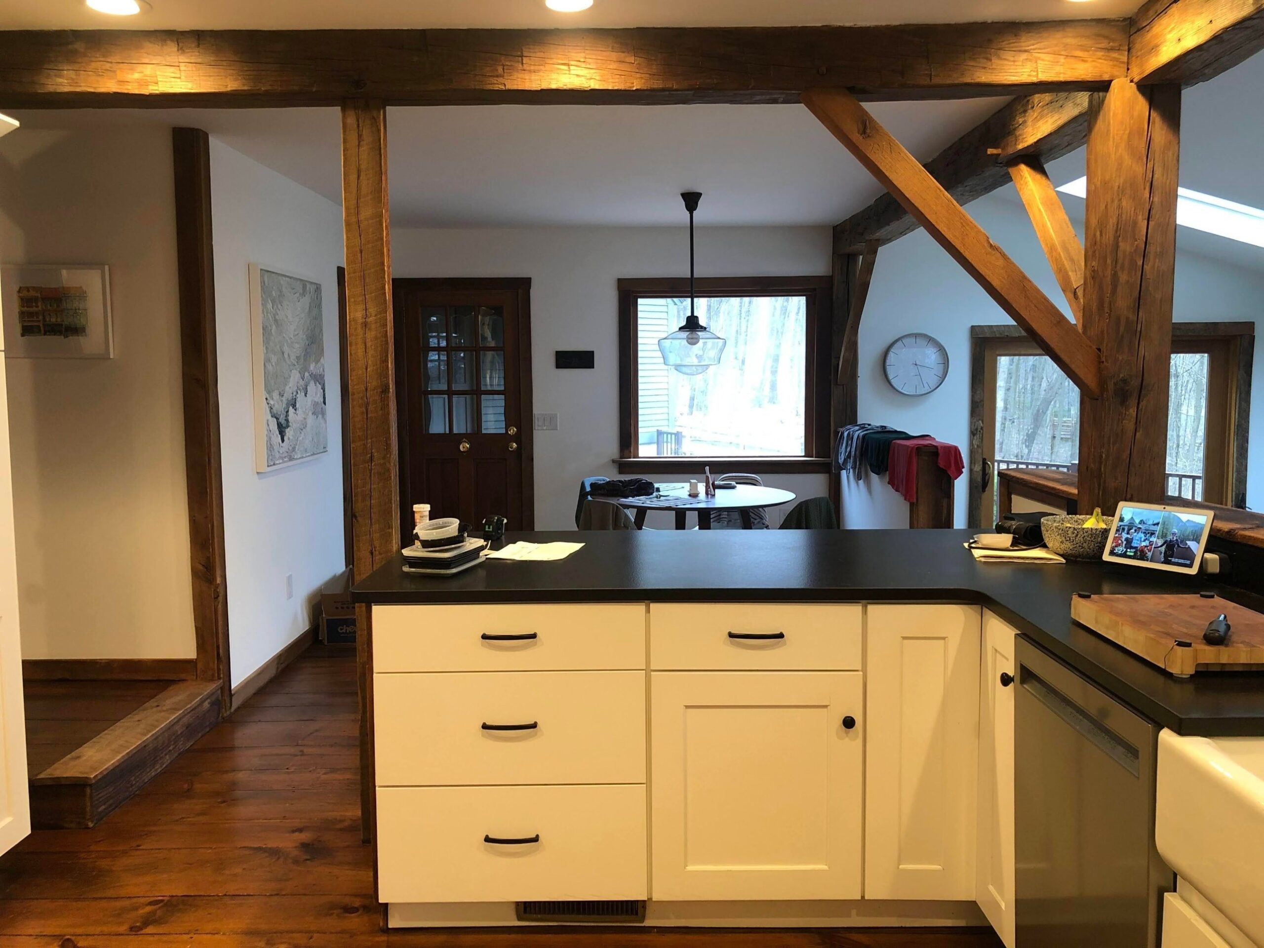 White Shaker peninsula with black counter, exposed wood posts and beams, and a view through to the dining nook and back door.