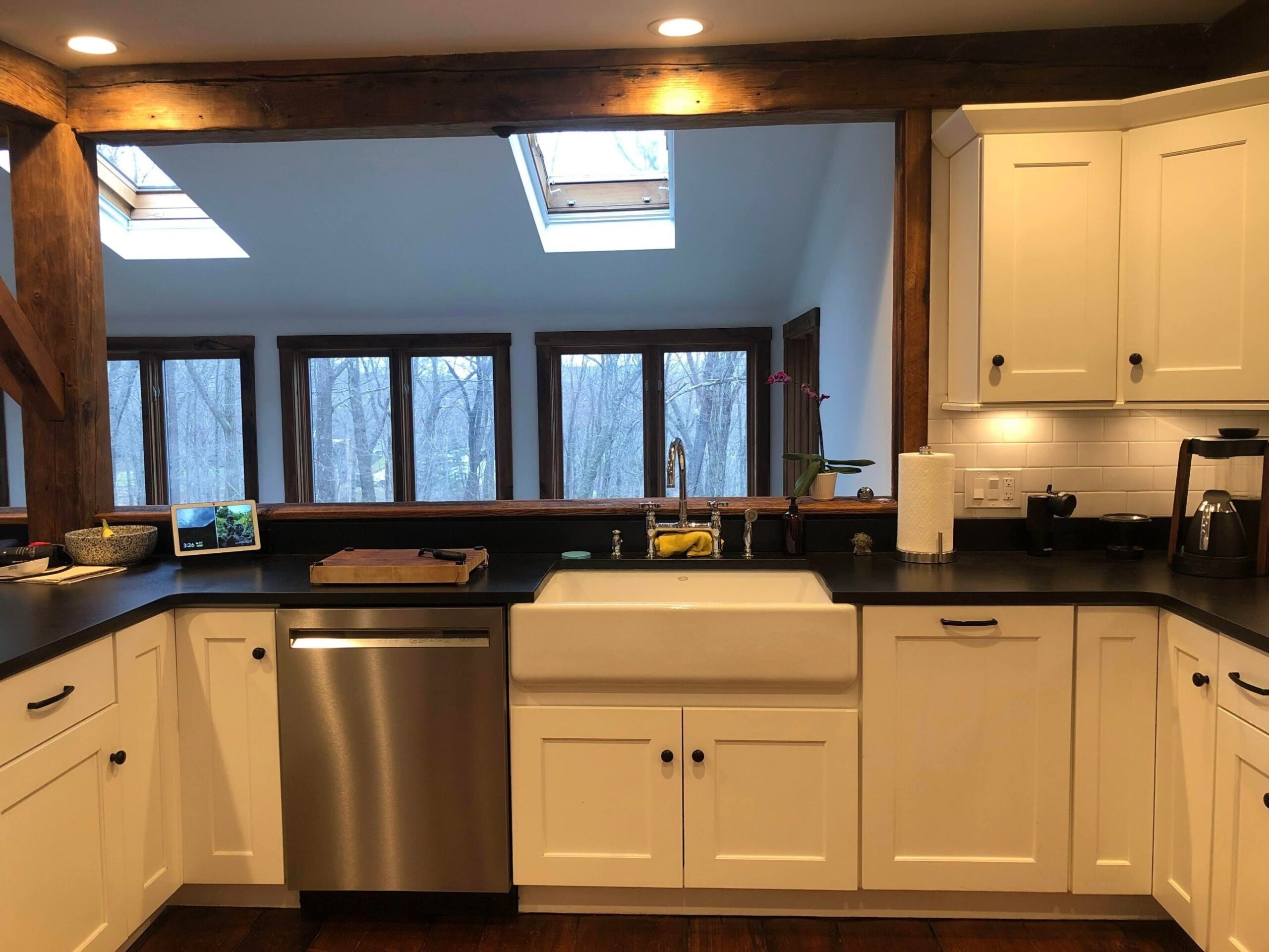 White Shaker cabinets, a farmhouse sink, black counters, and two skylights above a run of windows looking into bare winter trees.