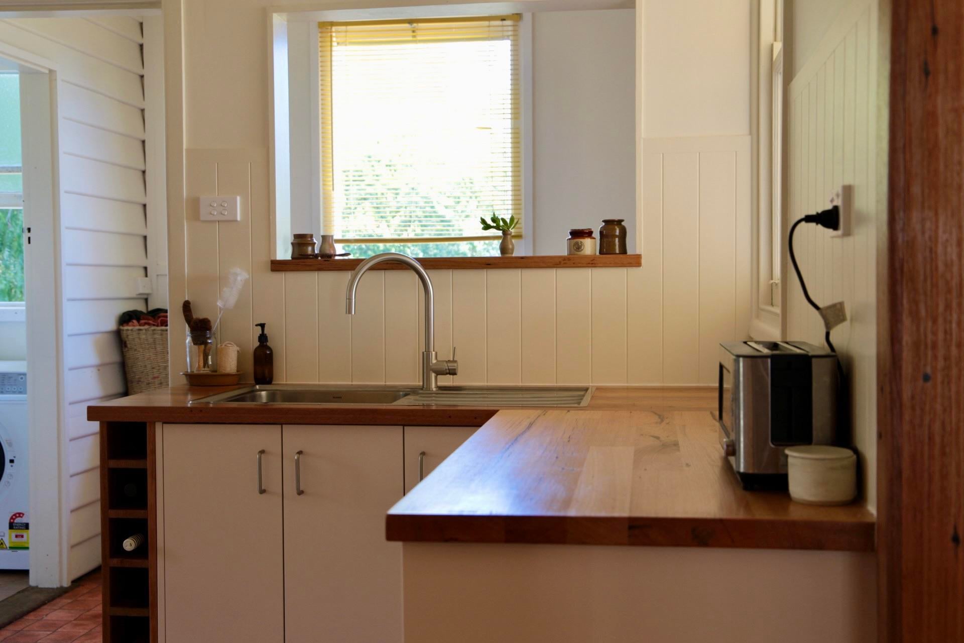 Bright kitchen sink corner with hardwood countertops, white cabinets, a pull-down faucet, white paneled walls, and a wood window ledge holding small pots.