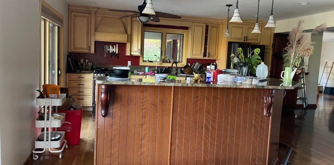 Wide-angle 16:9 view of a yellow glazed Tuscan kitchen with a cherry brown beadboard island, green granite counters, globe pendant lights, and burgundy accent walls before the Providence Blue paint makeover.